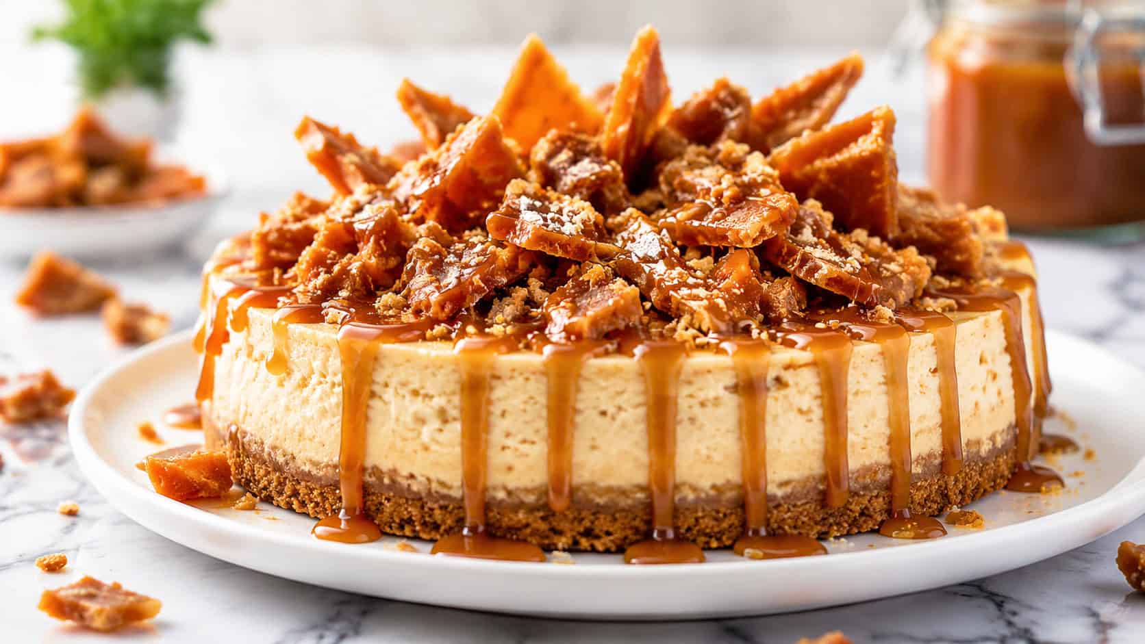 a toffee-loaded cheesecake piled high with crunchy toffee shards and caramel in a wide horizontal shot, on a white plate with scattered toffee pieces on a marble surface, bright crisp light, shallow depth of field, landscape orientation