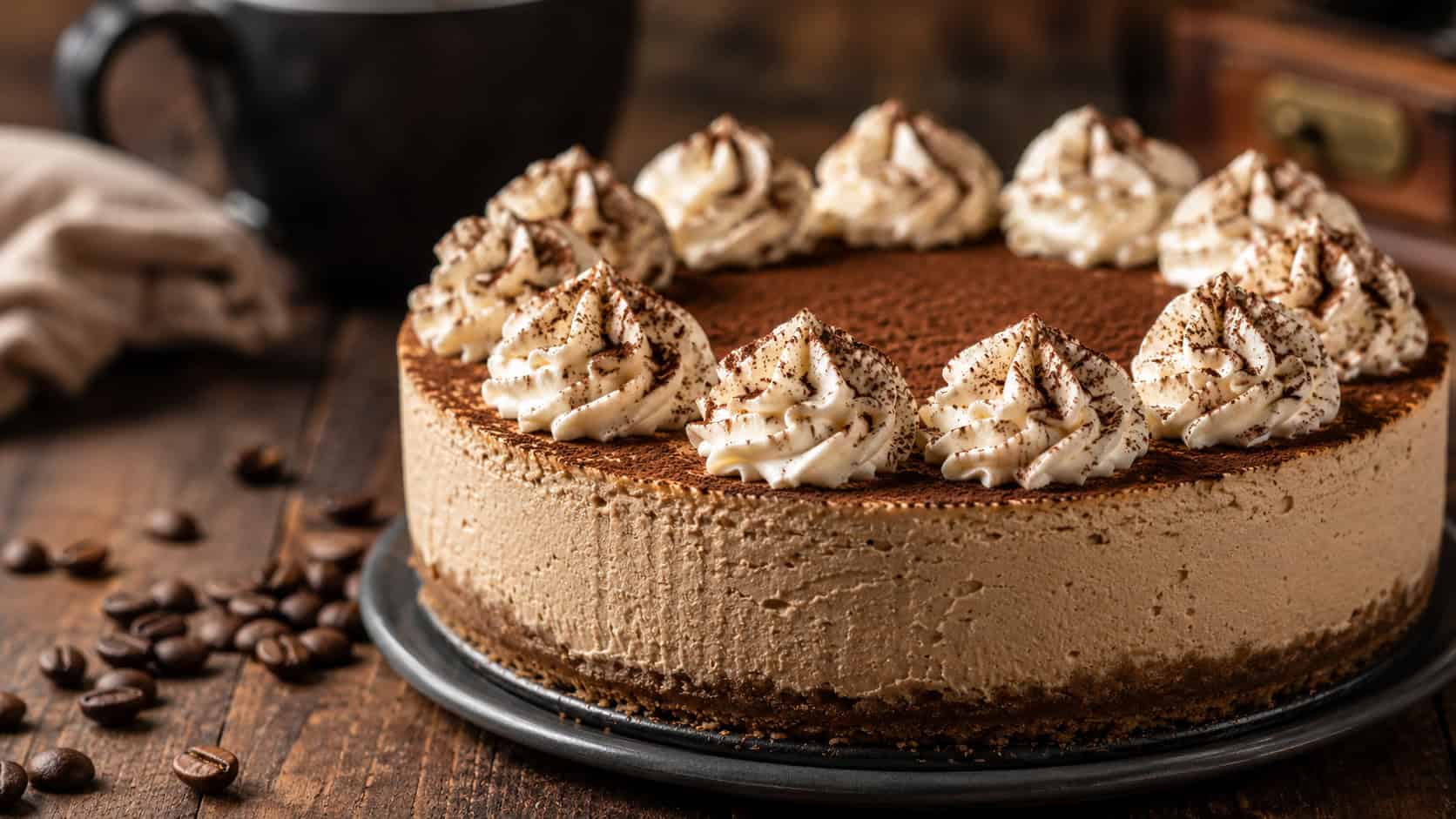 a mocha cheesecake dusted with cocoa and topped with whipped cream swirls in a wide horizontal shot, coffee beans scattered nearby, set on a dark wooden table, warm natural light, shallow depth of field, landscape orientation