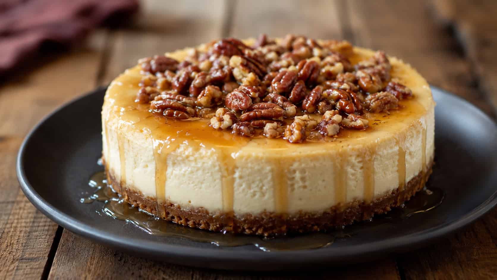 a maple cheesecake drizzled with syrup and topped with pecans in a wide horizontal shot, set on a dark plate on a rustic wooden table, warm natural light, shallow depth of field, landscape orientation