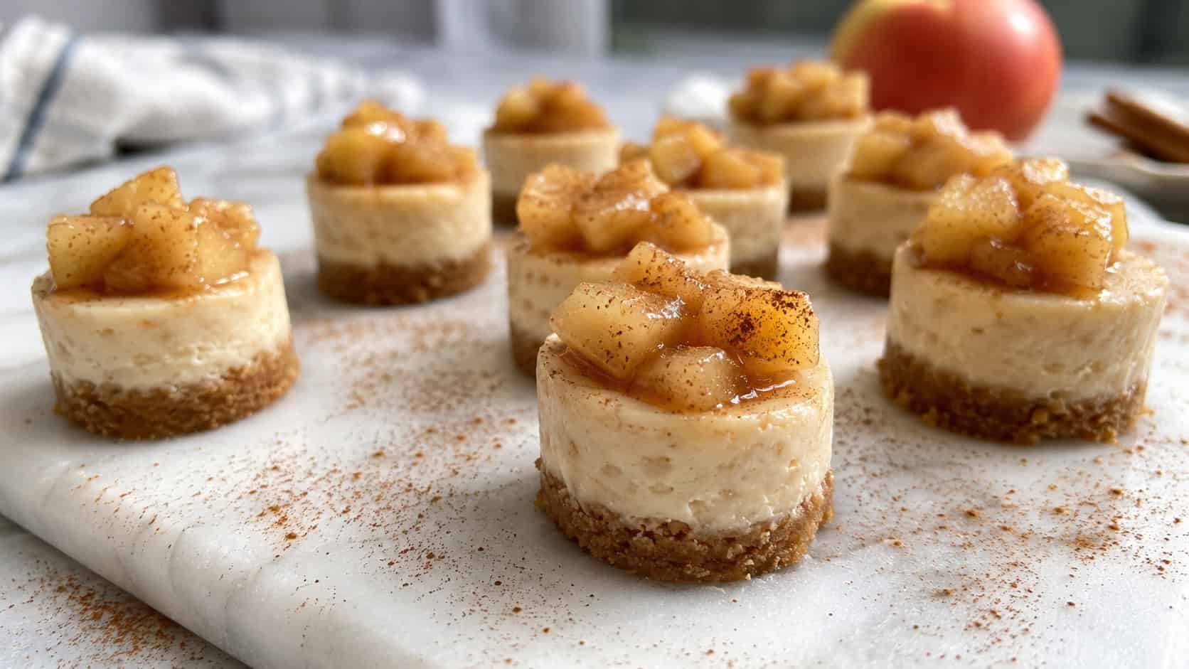 tiny cinnamon cheesecake bites topped with apple compote, in a wide horizontal shot on a marble tray dusted with cinnamon, natural light, shallow depth of field, landscape orientation