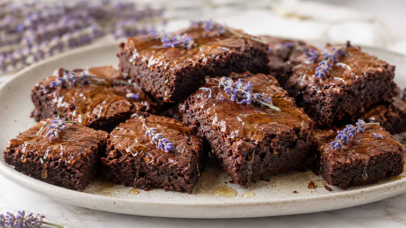 a wide horizontal arrangement of chocolate brownies drizzled with honey and a few sprigs of lavender on top, on a pale ceramic plate, soft bright natural light, shallow depth of field, landscape orientation