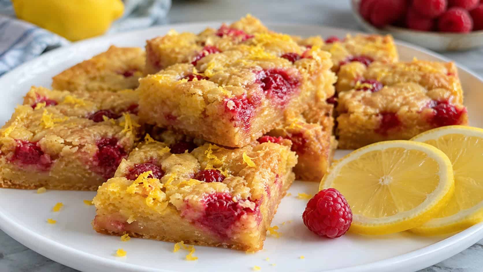 a wide horizontal arrangement of golden lemon blondies dotted with red raspberries and bright lemon zest, on a white plate with lemon slices, bright natural light, shallow depth of field, landscape orientation