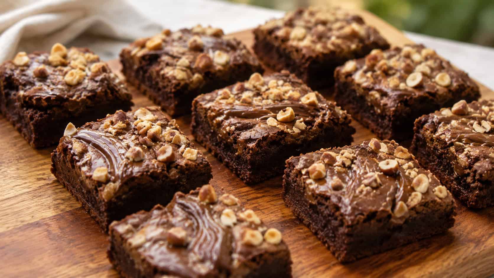 Nutella hazelnut brownies in a wide horizontal shot, glossy hazelnut swirls and chopped toasted nuts across fudgy squares, arranged on a warm wooden board, natural light, shallow depth of field, landscape orientation