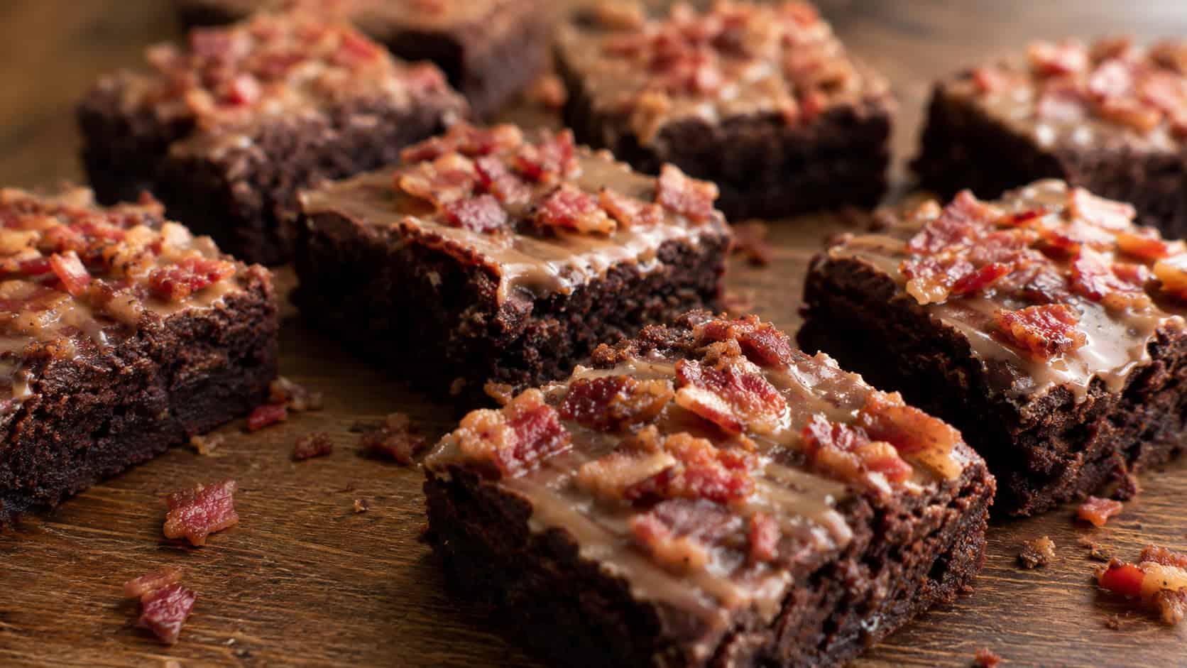 maple bacon brownies in a wide horizontal shot, fudgy squares scattered with crispy bacon crumbles and a thin maple glaze, on a dark wooden board, warm natural light, shallow depth of field, landscape orientation