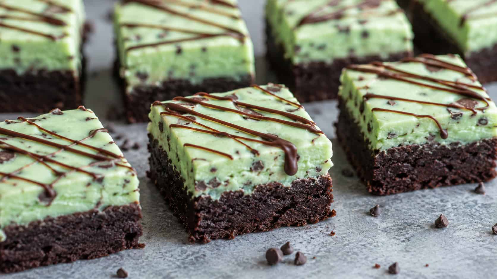 mint chocolate chip brownies in a wide horizontal shot, pale green mint layer over dark fudgy base with thin chocolate drizzle, squares arranged on a cool gray countertop, soft natural light, shallow depth of field, landscape orientation