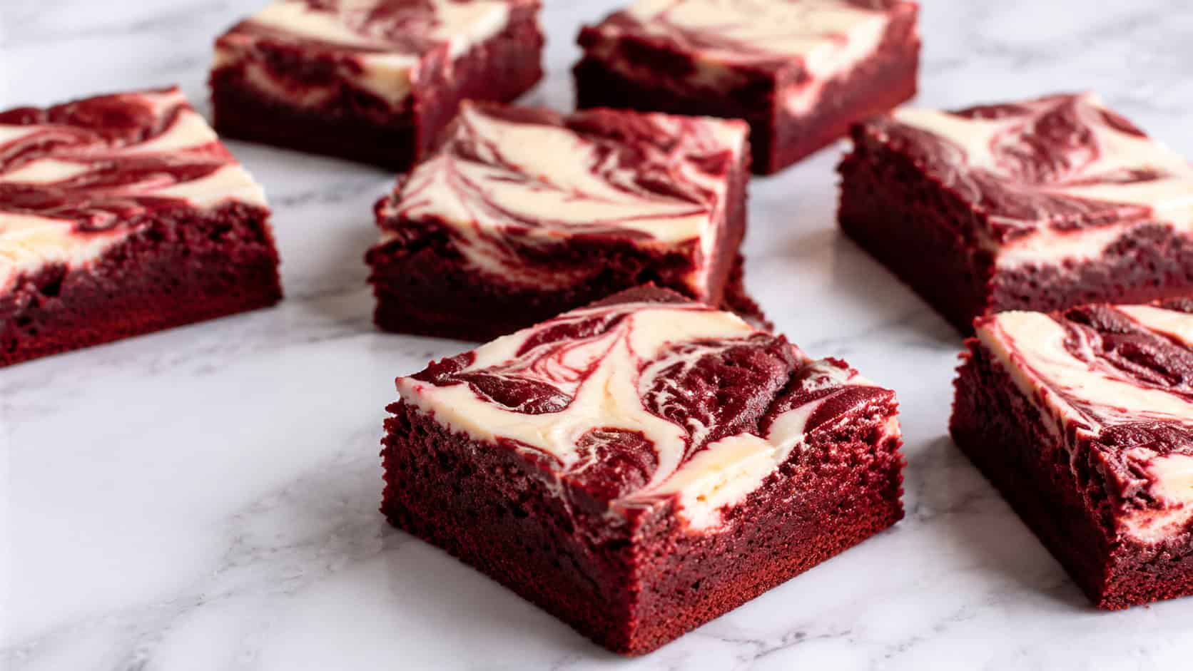 red velvet cream cheese brownies in a wide horizontal shot, deep crimson base with white cream cheese swirls, squares fanned out on a white marble surface, bright natural light, shallow depth of field, landscape orientation