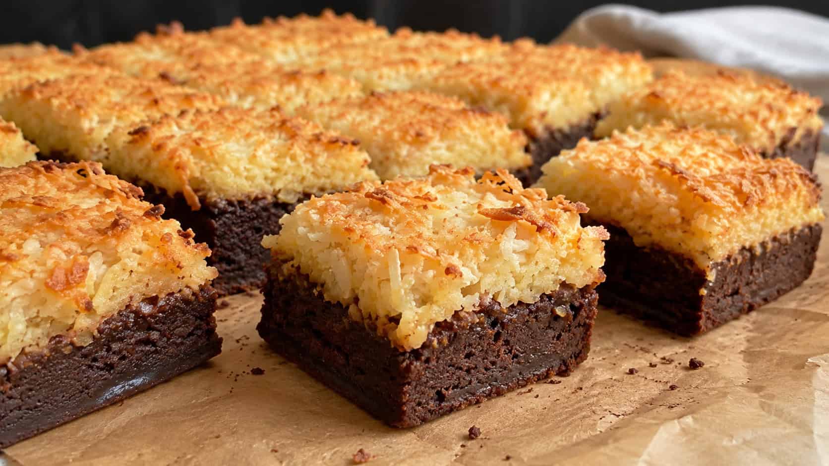 brownies topped with golden toasted coconut macaroon layer cut into squares on parchment, wide horizontal shot, fudgy chocolate base visible, natural light, shallow depth of field, landscape orientation