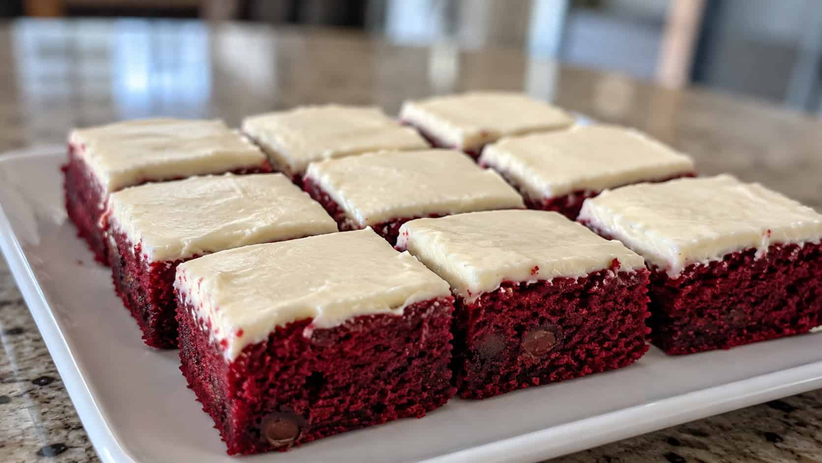 red velvet brownies topped with white cream cheese frosting cut into squares on a white plate, wide horizontal shot, vivid red interior visible, soft natural light, shallow depth of field, landscape orientation