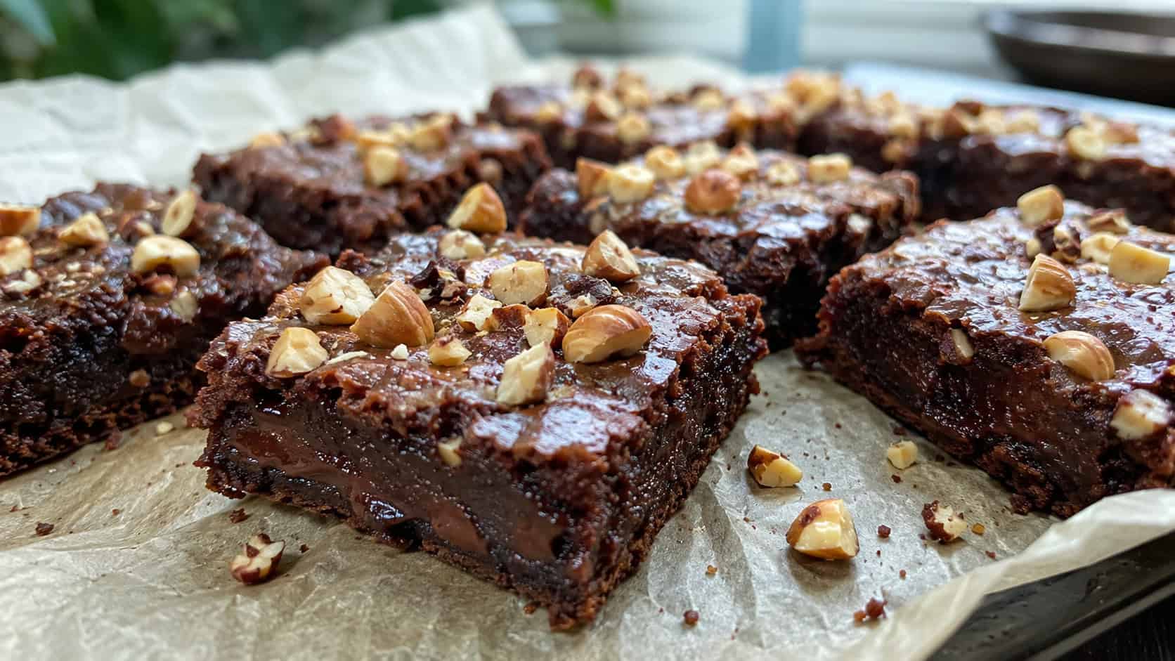 fudgy hazelnut brownies topped with chopped toasted hazelnuts on parchment, wide horizontal shot, glossy surface and gooey center, natural light, shallow depth of field, landscape orientation