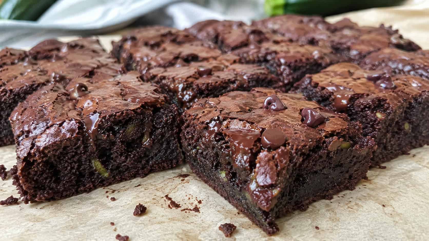 moist chocolate zucchini brownies cut into squares on parchment with melty chips, wide horizontal shot, dense fudgy interior visible, natural light, shallow depth of field, landscape orientation