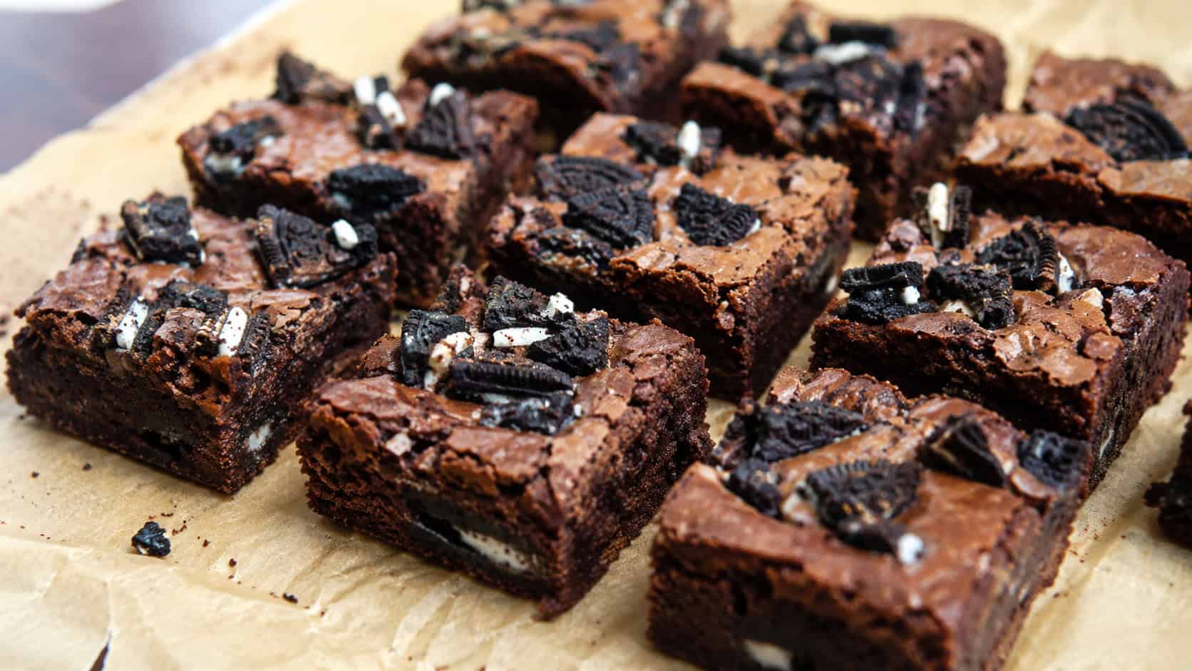 fudgy brownies topped with crushed chocolate sandwich cookie pieces cut into squares on parchment, wide horizontal shot, cookie chunks visible inside, natural light, shallow depth of field, landscape orientation
