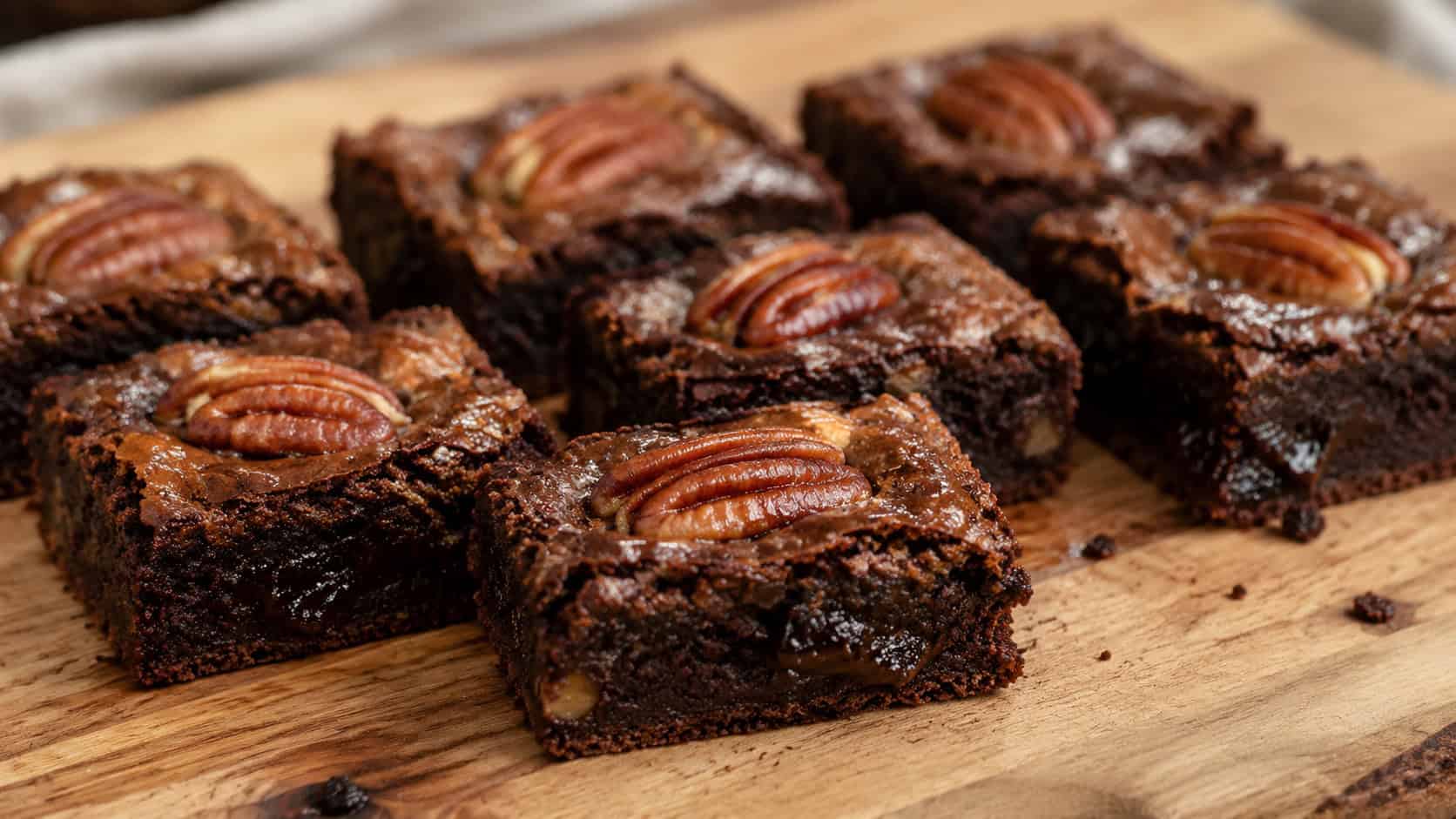 fudgy maple brownies topped with toasted pecan halves cut into squares on a wooden board, wide horizontal shot, glossy surface and gooey center, warm natural light, shallow depth of field, landscape orientation