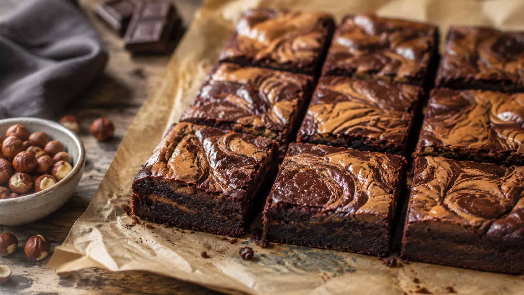 fudgy brownies with marbled hazelnut swirls on top, cut into squares on parchment, wide horizontal shot, glossy surface, rustic table, natural light, shallow depth of field, landscape orientation