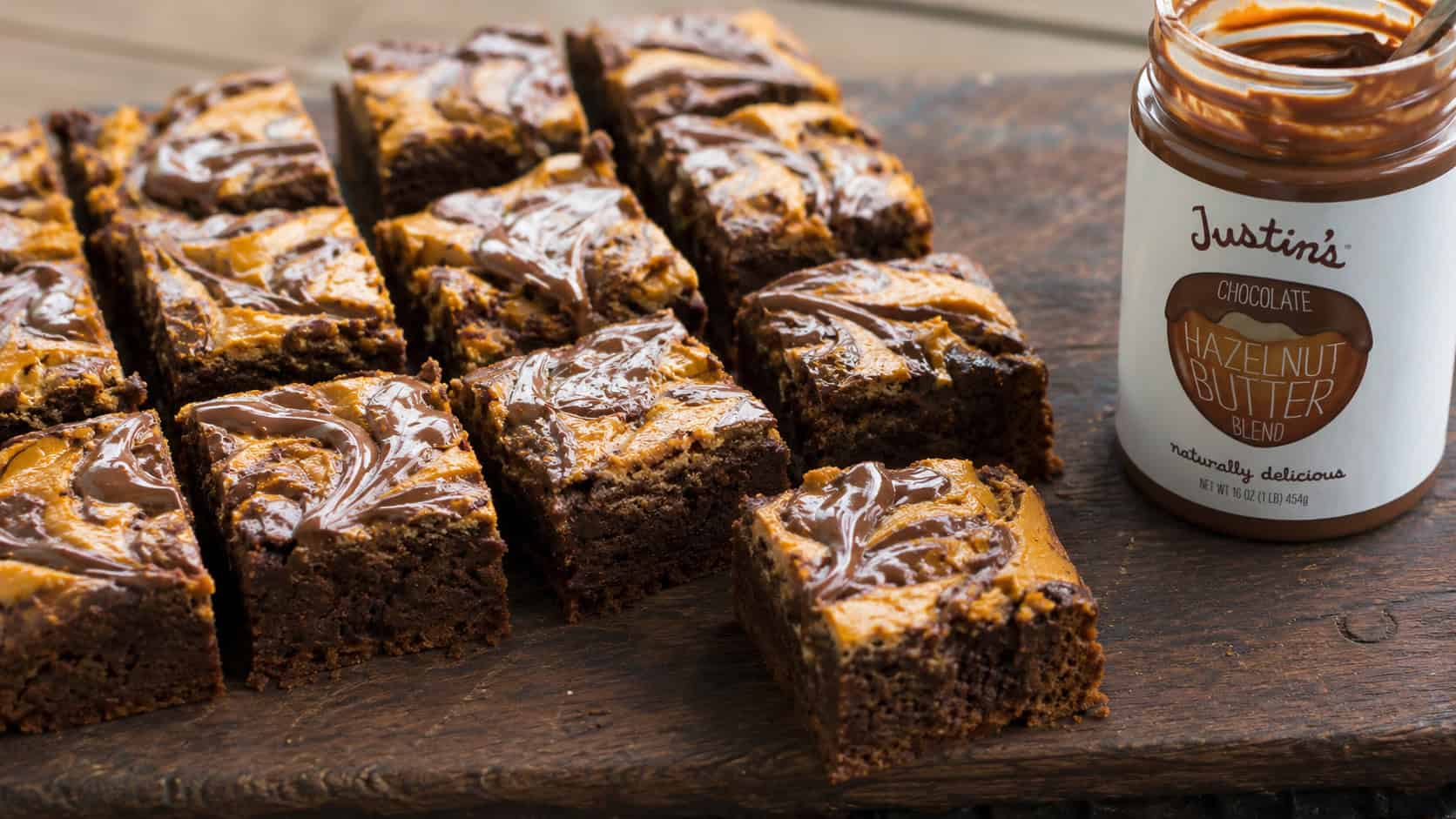 pumpkin brownies with glossy chocolate hazelnut swirls cut into squares, in a wide horizontal shot on a dark wooden board with a jar nearby, natural light, shallow depth of field, landscape orientation