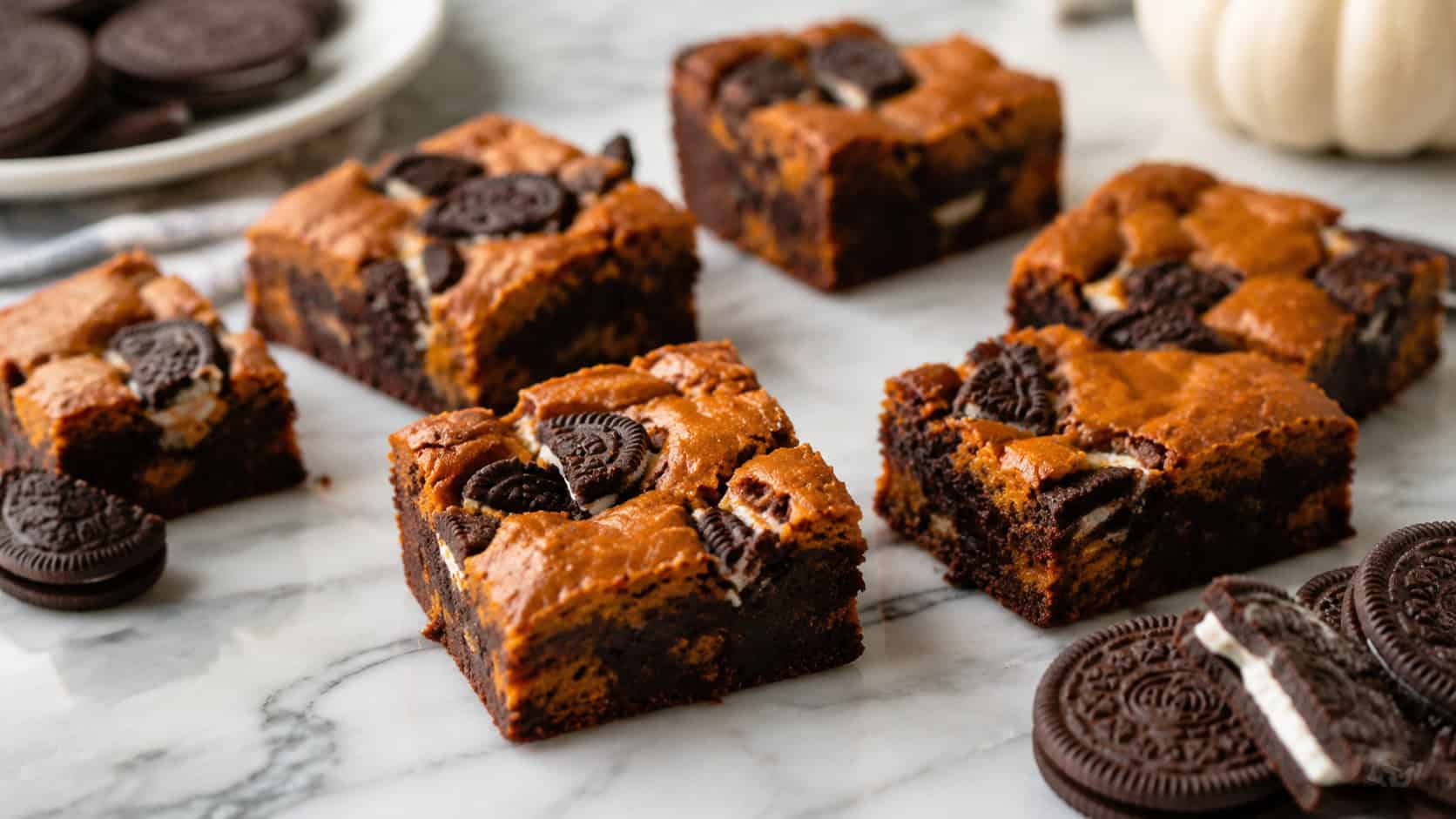 pumpkin brownies studded with chunks of chocolate sandwich cookies cut into squares, in a wide horizontal shot on a marble surface with extra cookies, natural light, shallow depth of field, landscape orientation