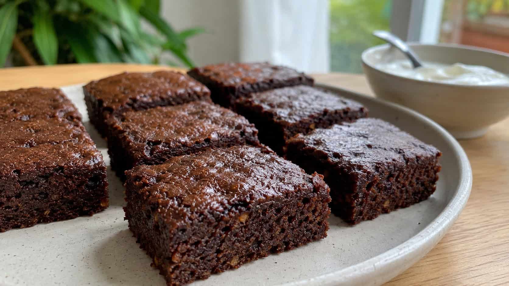 dark moist pumpkin brownies cut into neat squares, in a wide horizontal shot on a light ceramic plate with a small bowl of yogurt nearby, natural light, shallow depth of field, landscape orientation