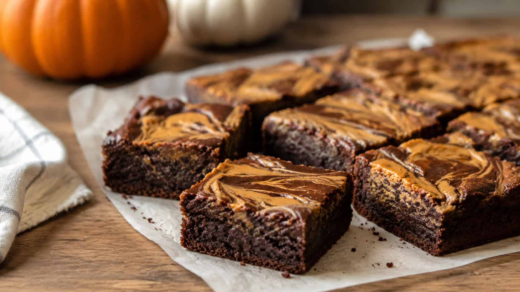 fudgy pumpkin brownies with swirls of peanut butter cut into squares, in a wide horizontal shot on parchment over a wooden table, natural light, shallow depth of field, landscape orientation