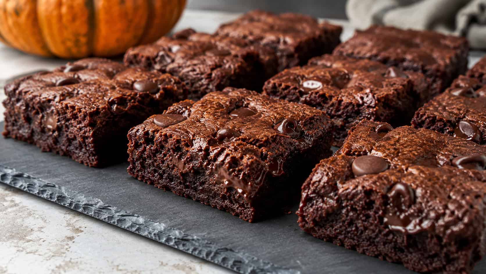 dark moist chocolate pumpkin brownies cut into squares with melty chocolate chips, in a wide horizontal shot on a slate board, natural light, shallow depth of field, landscape orientation