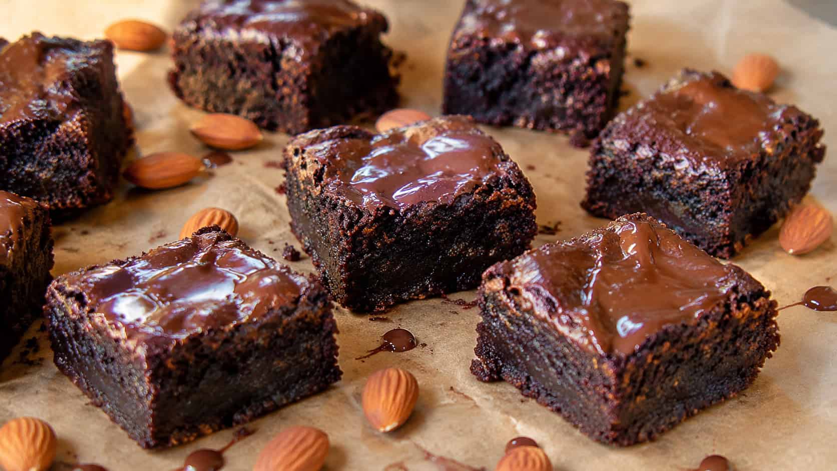 fudgy dark vegan pumpkin brownies cut into squares with glossy melted chocolate, in a wide horizontal shot on parchment with scattered almonds, natural light, shallow depth of field, landscape orientation