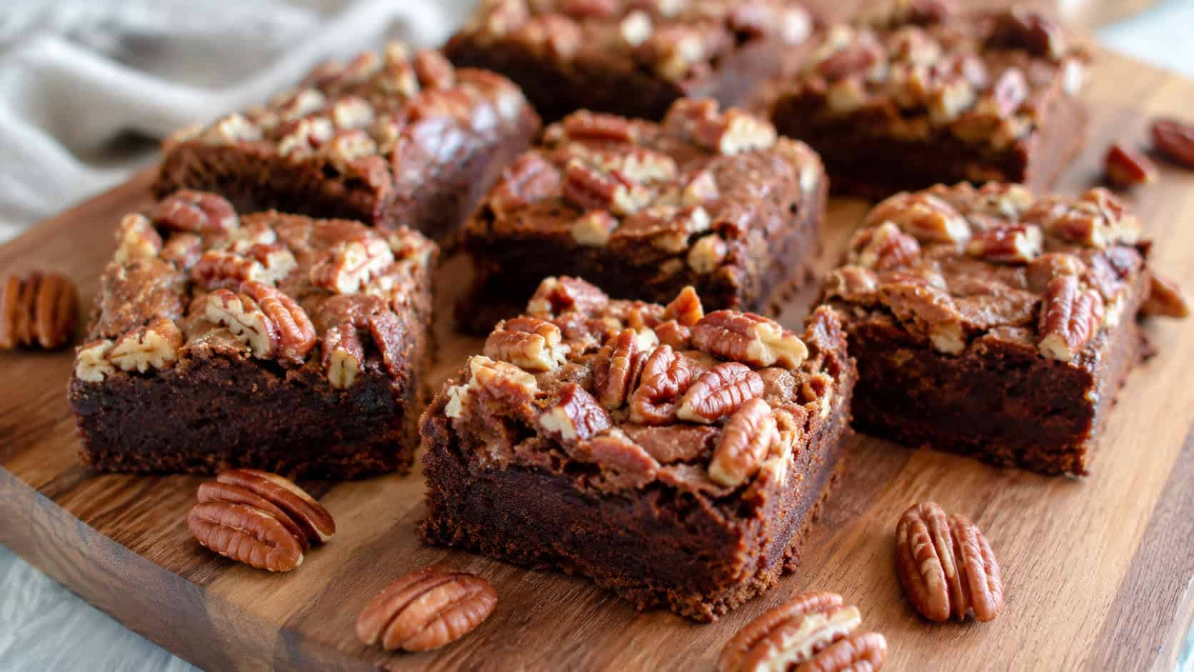 fudgy pumpkin brownies topped with caramelized pecans cut into squares, in a wide horizontal shot on a wooden board with whole pecans scattered around, natural light, shallow depth of field, landscape orientation