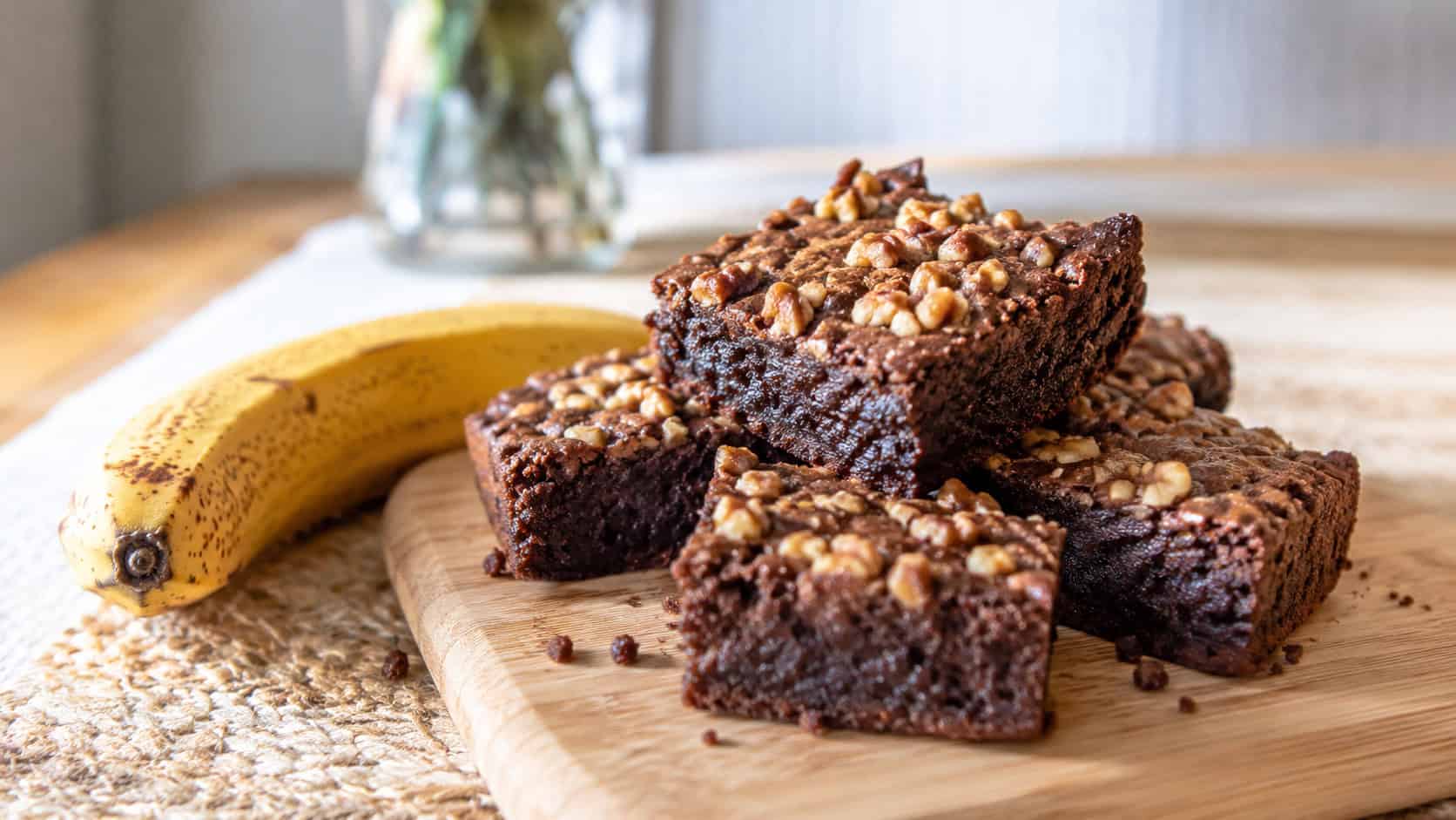 chocolate brownies topped with chopped walnuts and a fudgy crumb in a wide horizontal shot, on a wooden board beside a ripe banana on a cozy table, natural light, shallow depth of field, landscape orientation