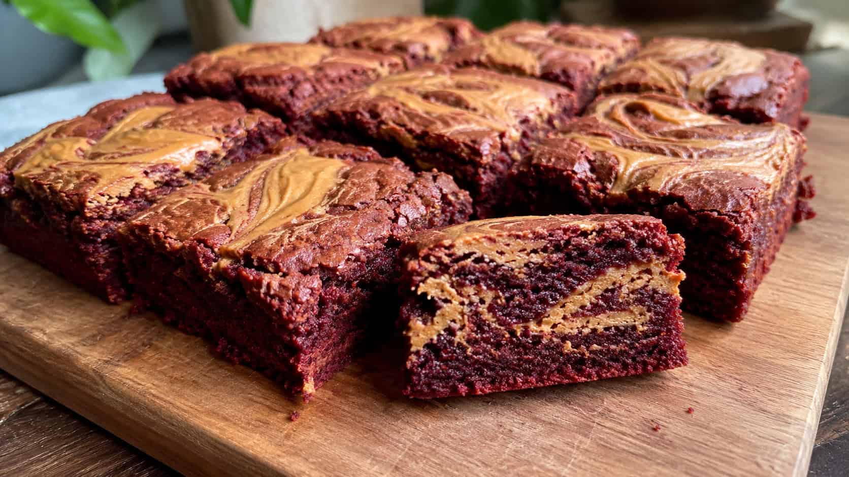 a wide horizontal arrangement of red velvet brownies with golden peanut butter swirls on top, one cut to show the marbling, on a wooden board, natural light, shallow depth of field, landscape orientation