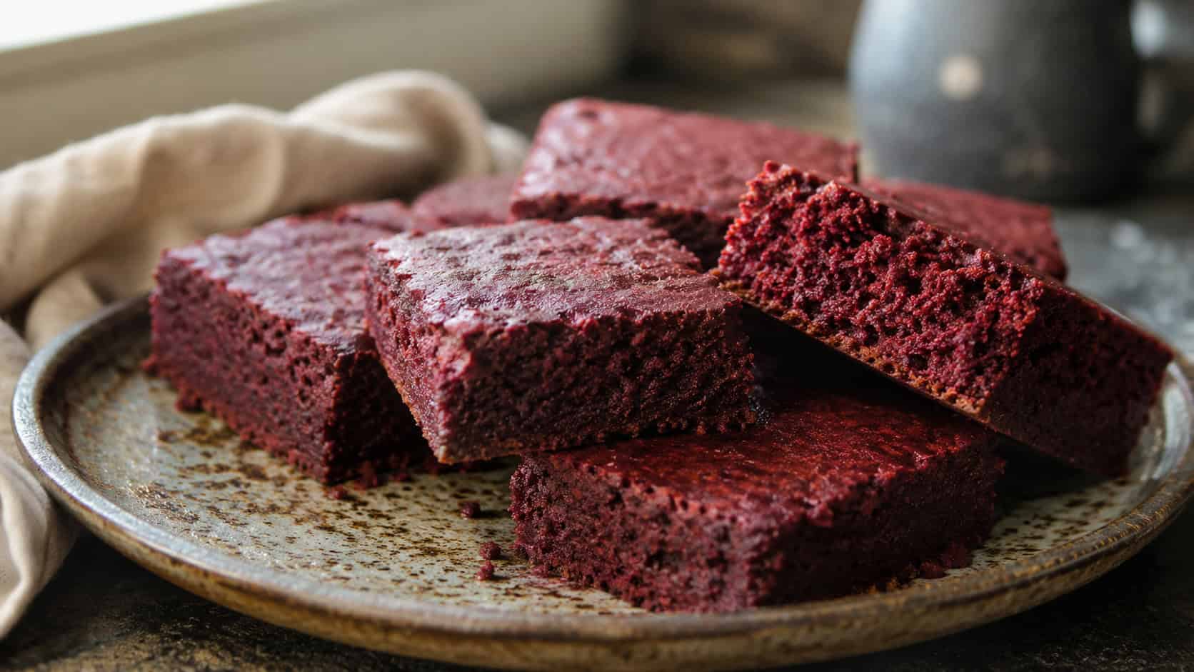 a wide horizontal plate of deep red gluten-free brownies with a tender crumb, one piece showing the soft interior, on a rustic ceramic plate, natural light, shallow depth of field, landscape orientation