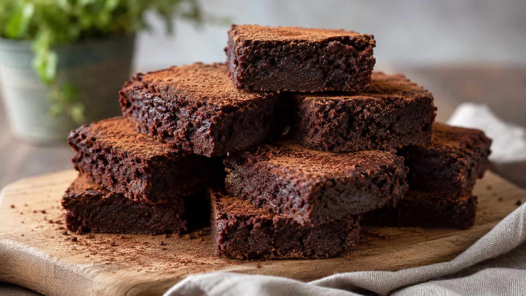 a wide horizontal stack of dark red vegan brownies with a soft fudgy texture, dusted lightly with cocoa, on a wooden board with a linen napkin, natural light, shallow depth of field, landscape orientation