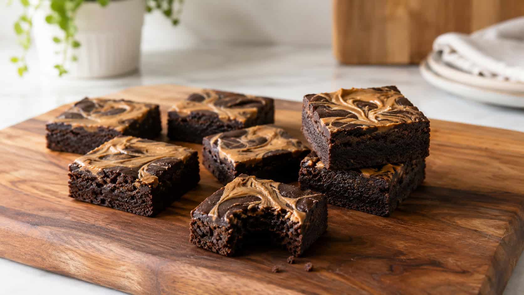 simple peanut butter brownie squares on a wide cutting board in a horizontal shot, neat dark squares with golden peanut butter swirls on top, a couple stacked and one bitten on a clean bright counter, natural light, shallow depth of field, landscape orientation