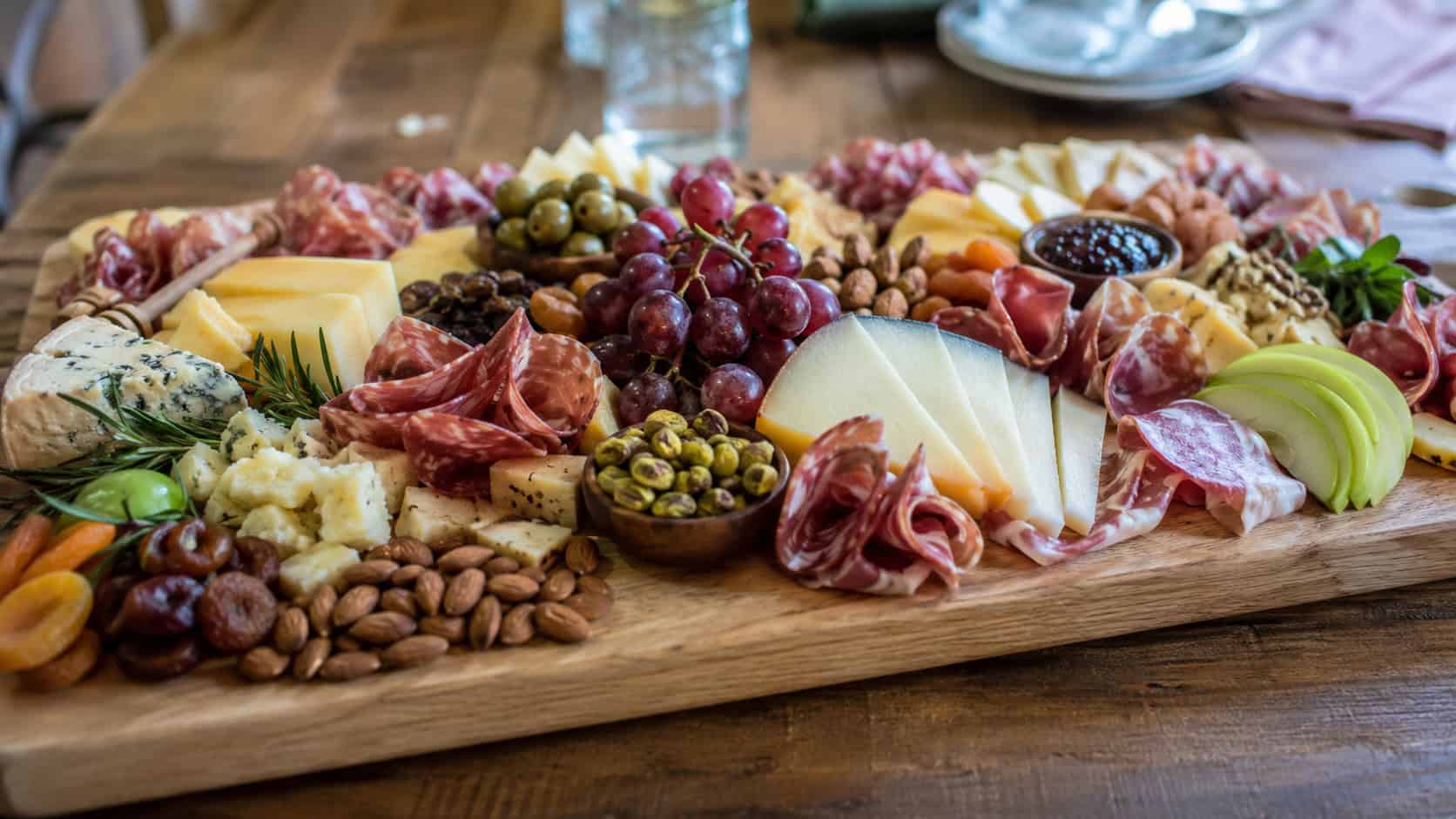 an abundant charcuterie board with cheeses, folded meats, grapes, apples, and nuts in a wide horizontal shot, on a large wooden board over a rustic table, natural light, shallow depth of field, landscape orientation