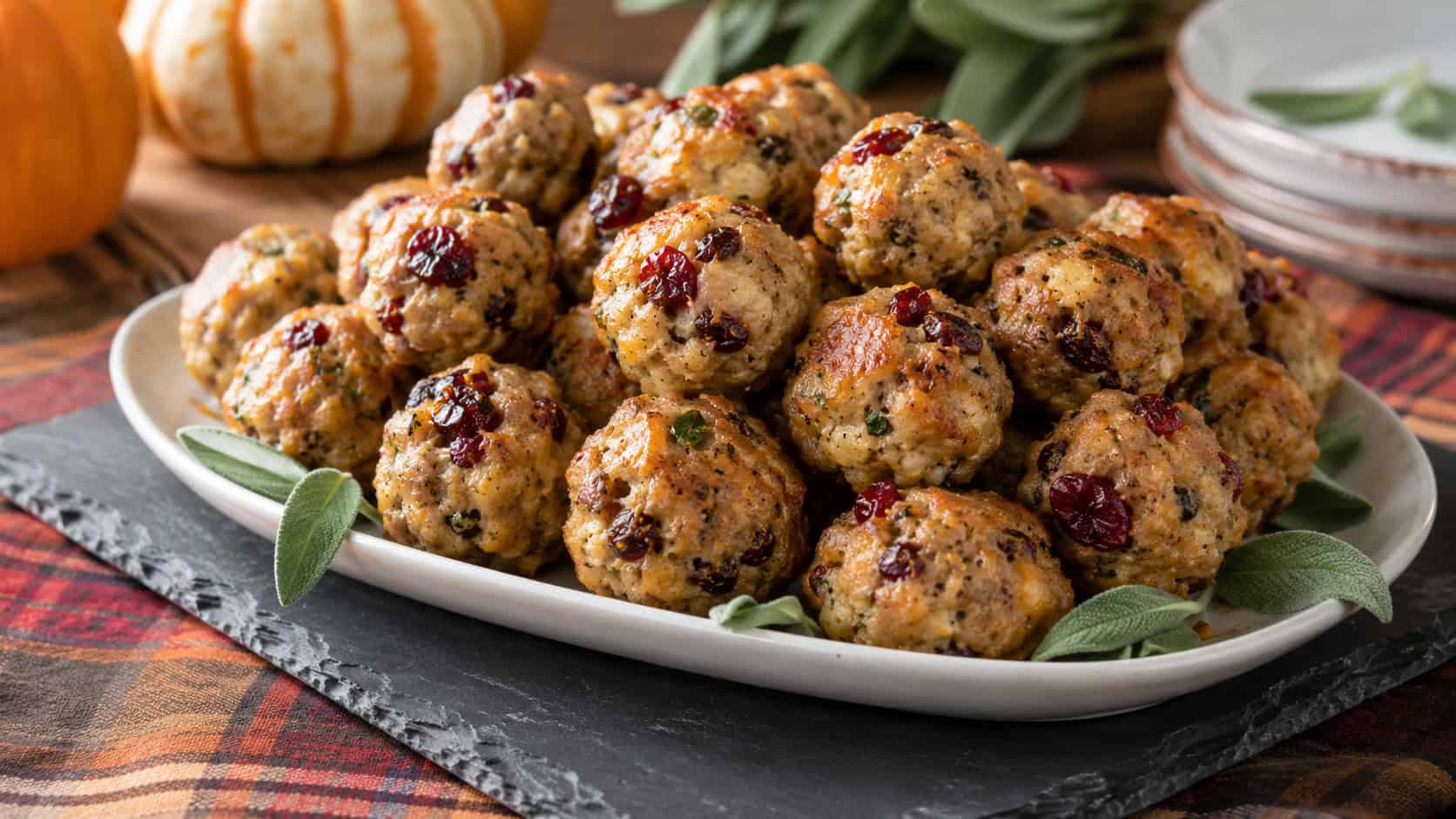 golden baked sausage balls flecked with cranberries and sage piled on a platter in a wide horizontal shot, on a slate board over a fall cloth, natural light, shallow depth of field, landscape orientation