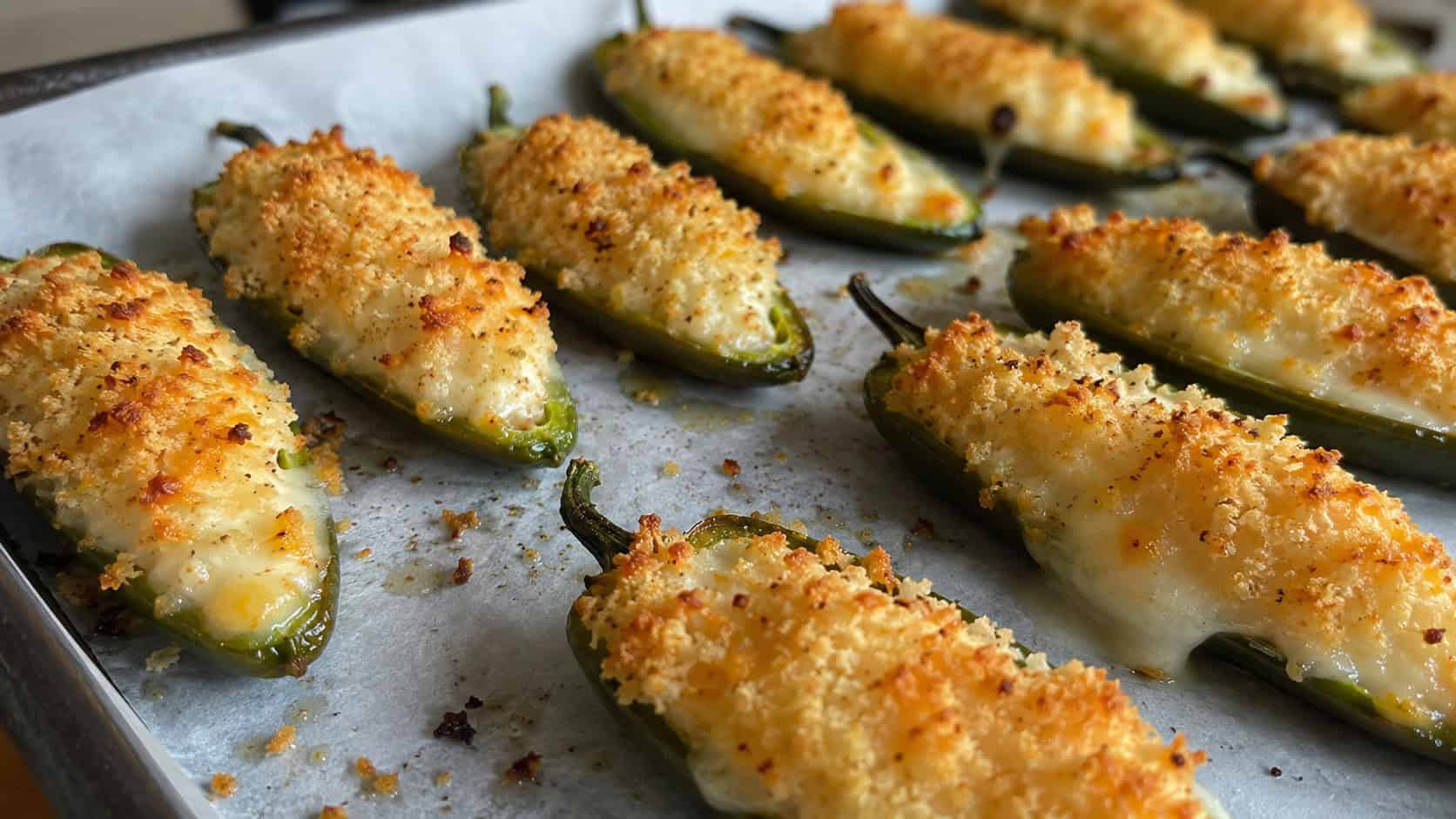 cheese stuffed jalapeños with golden breadcrumb tops and bubbling cheese in a wide horizontal shot, lined up on a parchment-lined tray, natural light, shallow depth of field, landscape orientation