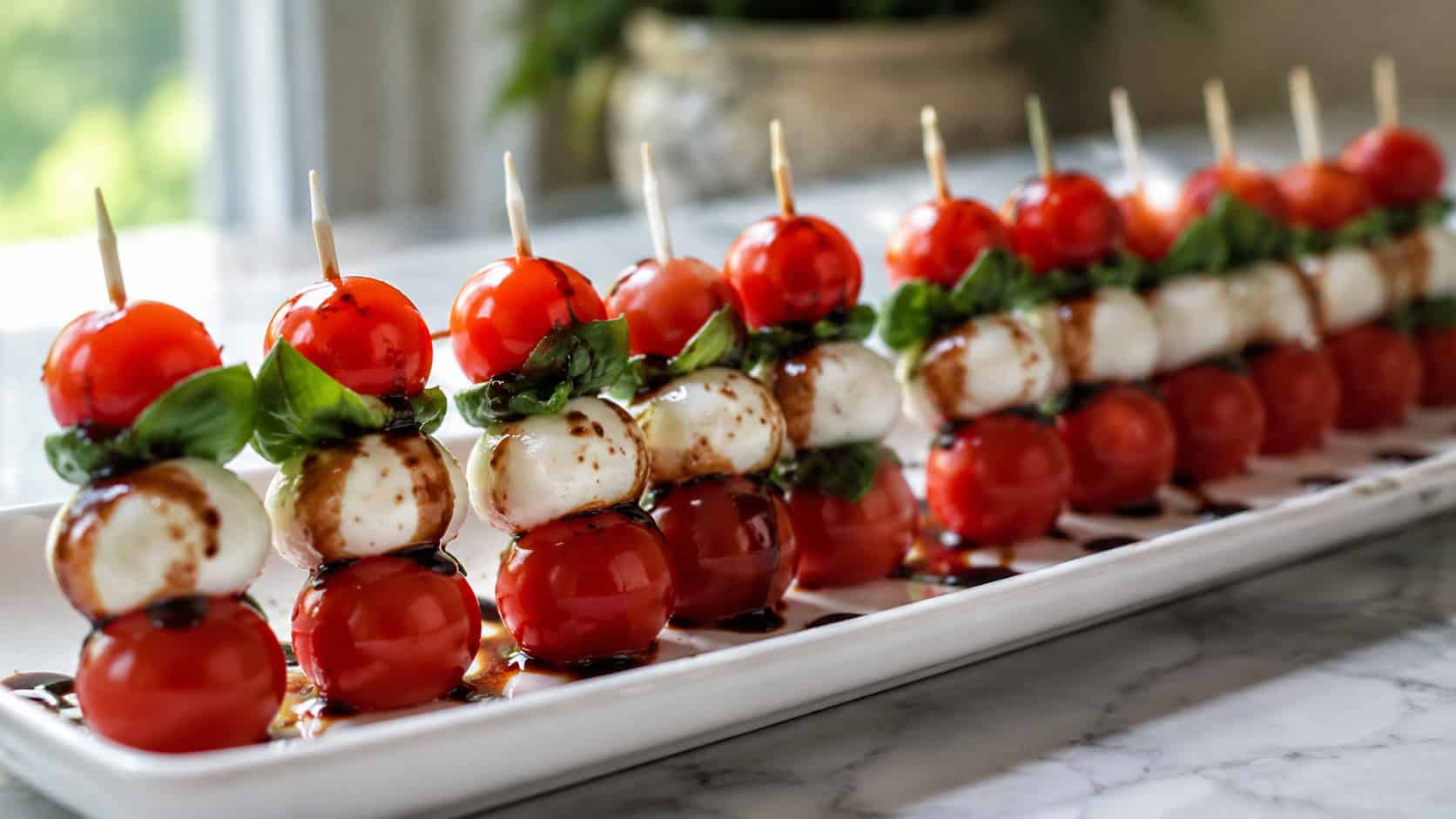 mini caprese skewers with bright red tomatoes, white mozzarella, and green basil drizzled with balsamic glaze in a wide horizontal shot, lined up on a long white platter, natural light, shallow depth of field, landscape orientation