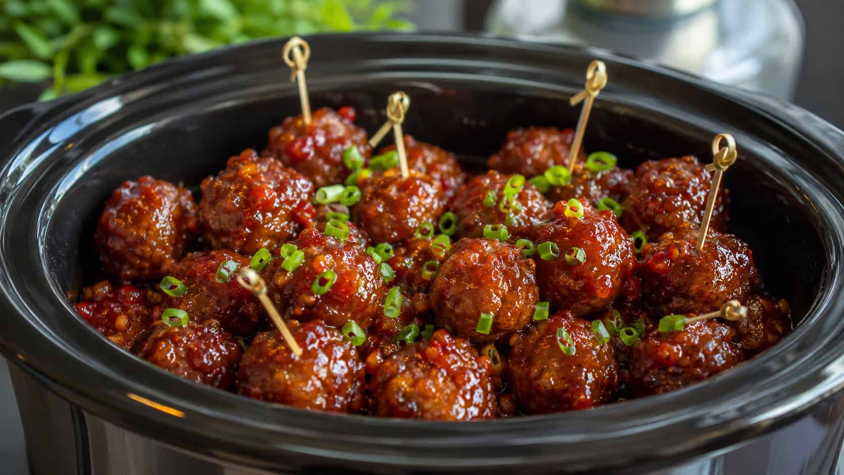 glossy sweet and spicy meatballs glazed in red sauce and sprinkled with green onions in a wide horizontal shot, served in a slow cooker insert with cocktail picks, natural light, shallow depth of field, landscape orientation