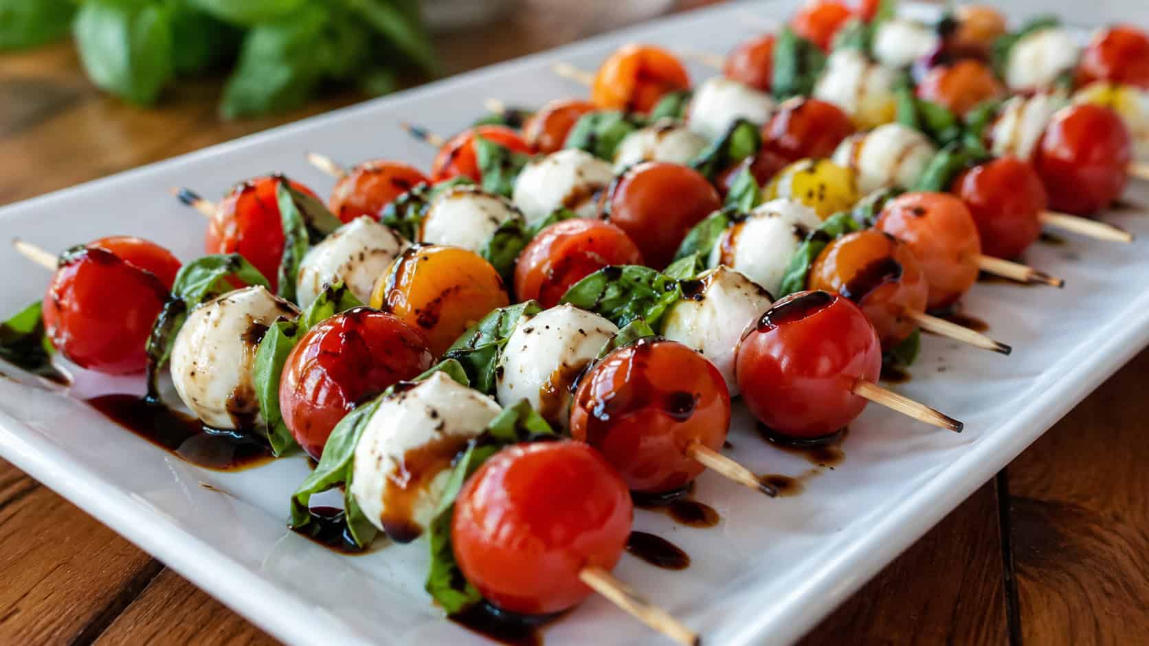 colorful caprese skewers in a wide horizontal shot, fanned across a long white platter with a balsamic drizzle and fresh basil, natural light, shallow depth of field, landscape orientation