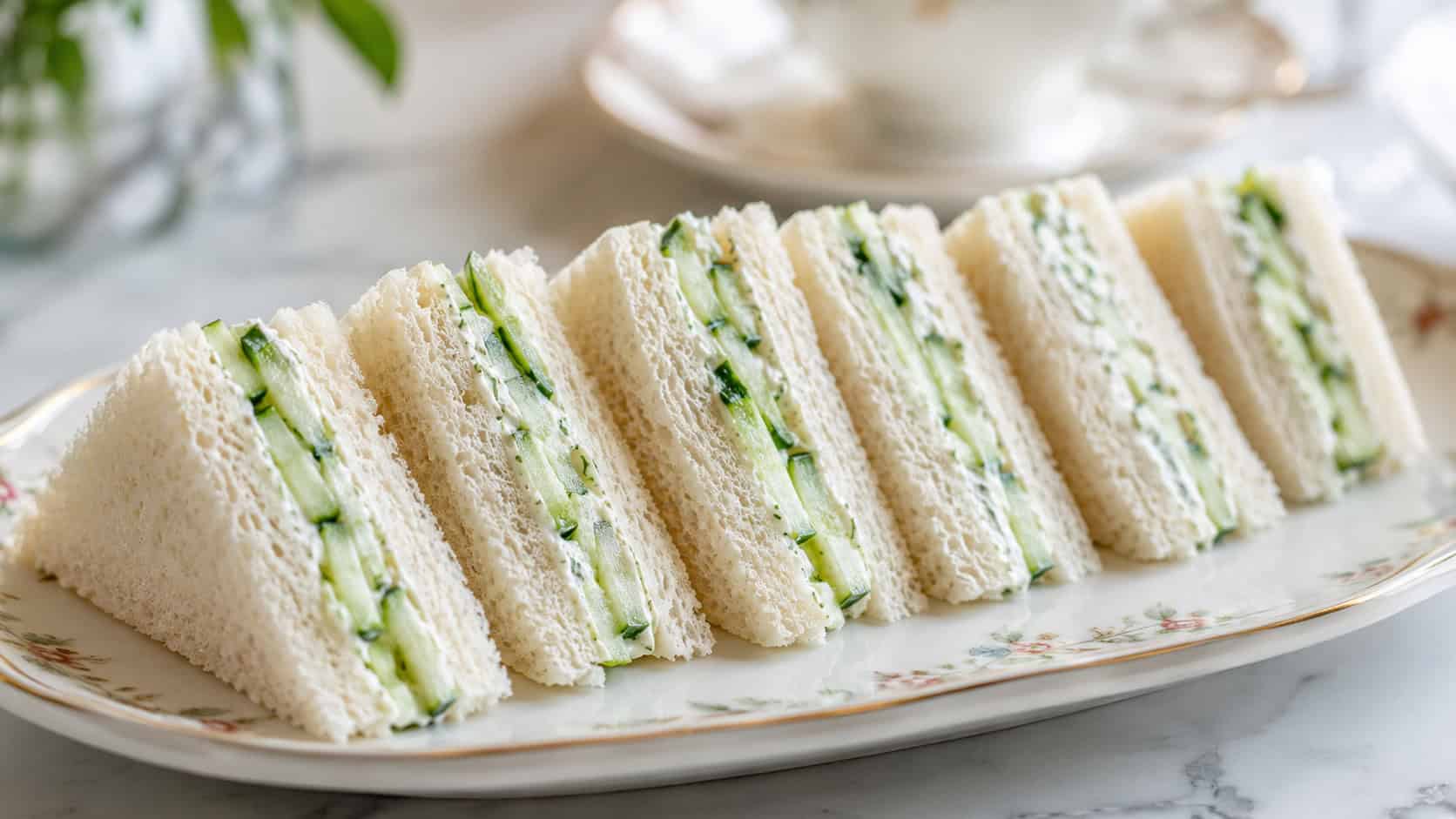 cucumber tea sandwiches cut into neat triangles showing creamy filling and cucumber, arranged in a wide horizontal row on a delicate plate, bright natural light, shallow depth of field, landscape orientation