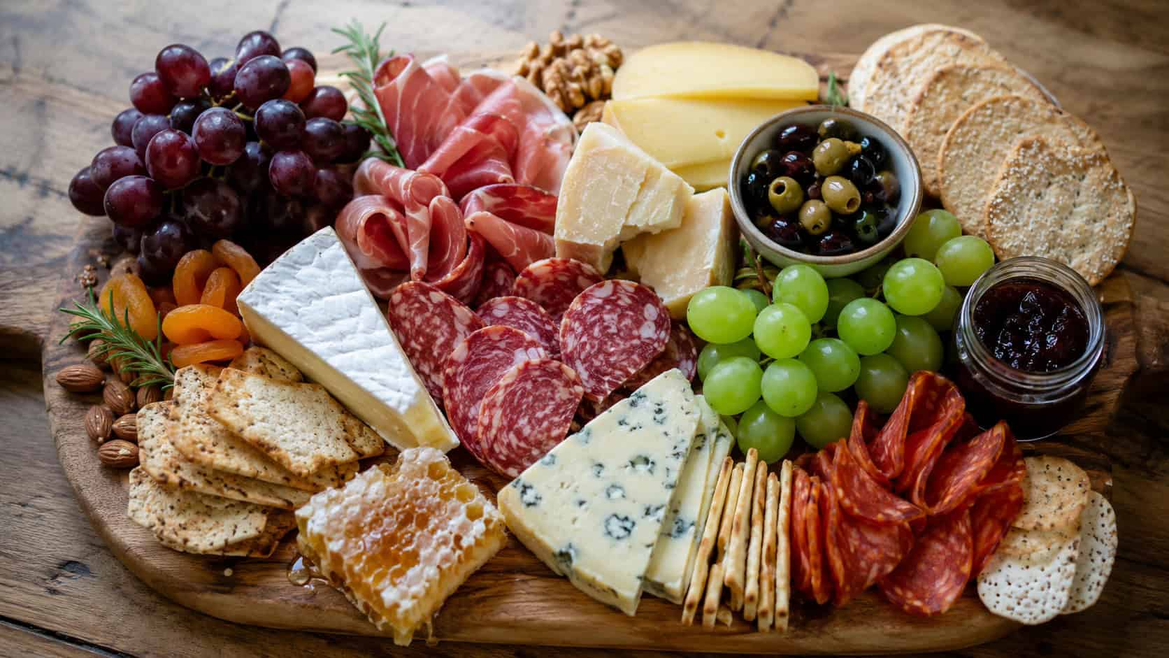 an abundant cheese and charcuterie board with cheeses, folded cured meats, grapes, nuts, and crackers, in a wide horizontal overhead shot on a rustic wooden board, natural light, shallow depth of field, landscape orientation