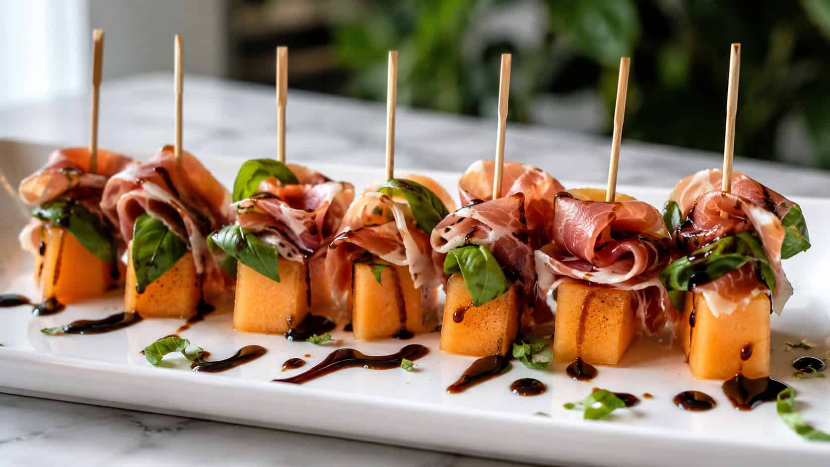 prosciutto and melon skewers with orange cantaloupe and green basil drizzled with balsamic, arranged in a wide horizontal row on a white platter, bright natural light, shallow depth of field, landscape orientation
