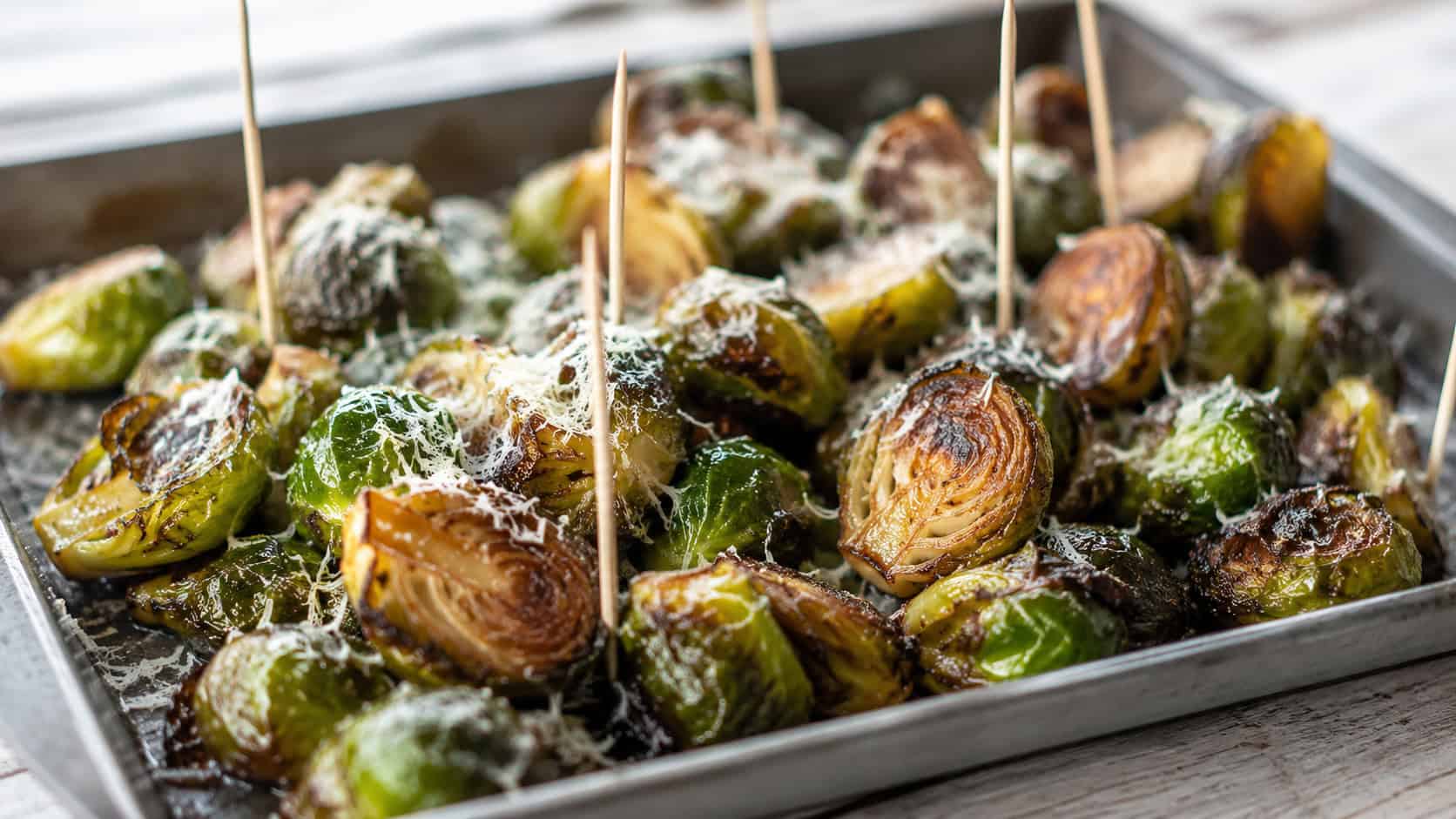 crispy caramelized Brussels sprouts glazed and sprinkled with parmesan, in a wide horizontal shot on a metal serving tray with toothpicks, natural light, shallow depth of field, landscape orientation
