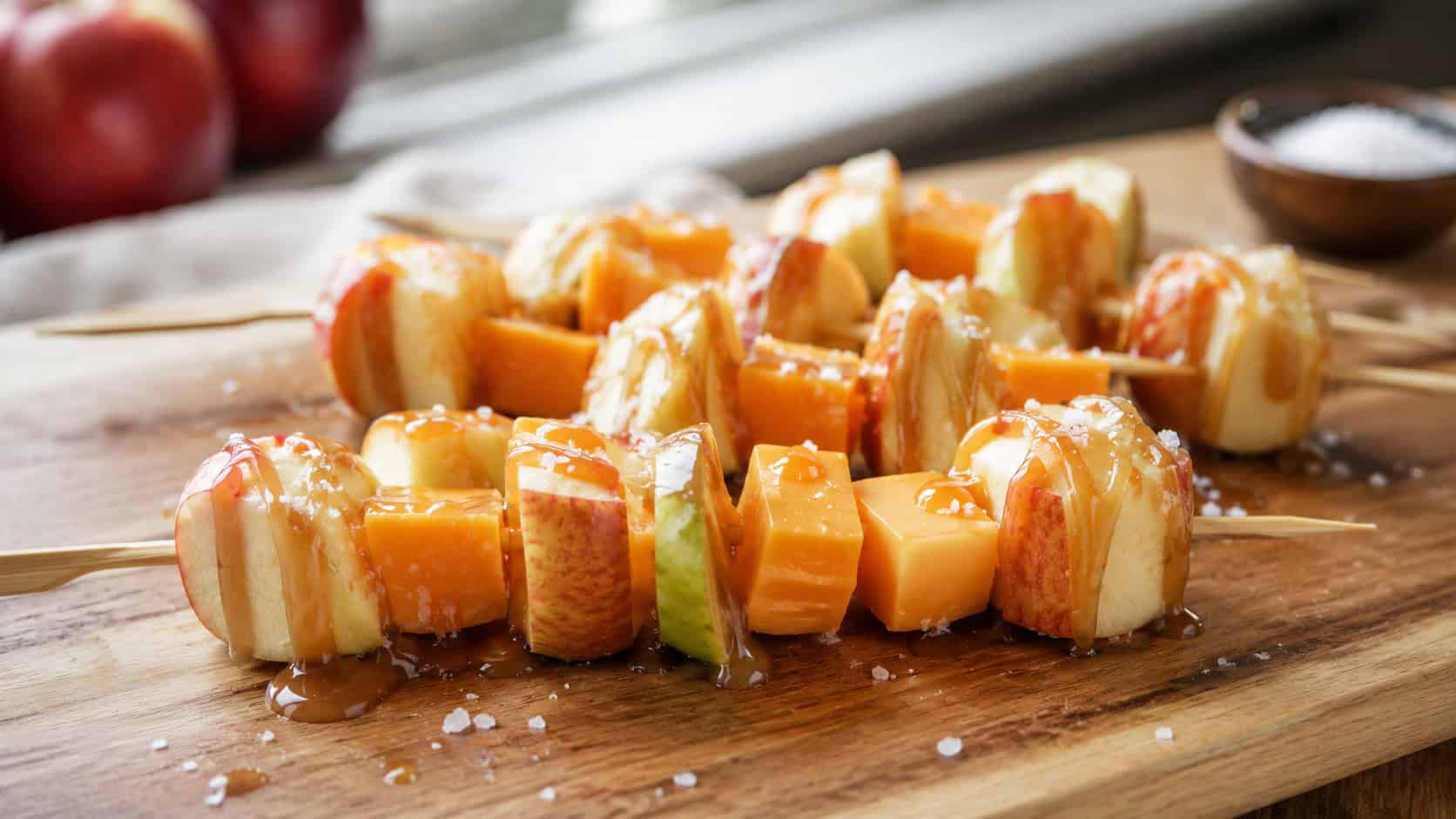 skewers of apple chunks and cheddar cubes drizzled with caramel and sea salt, in a wide horizontal shot on a wooden board, natural light, shallow depth of field, landscape orientation