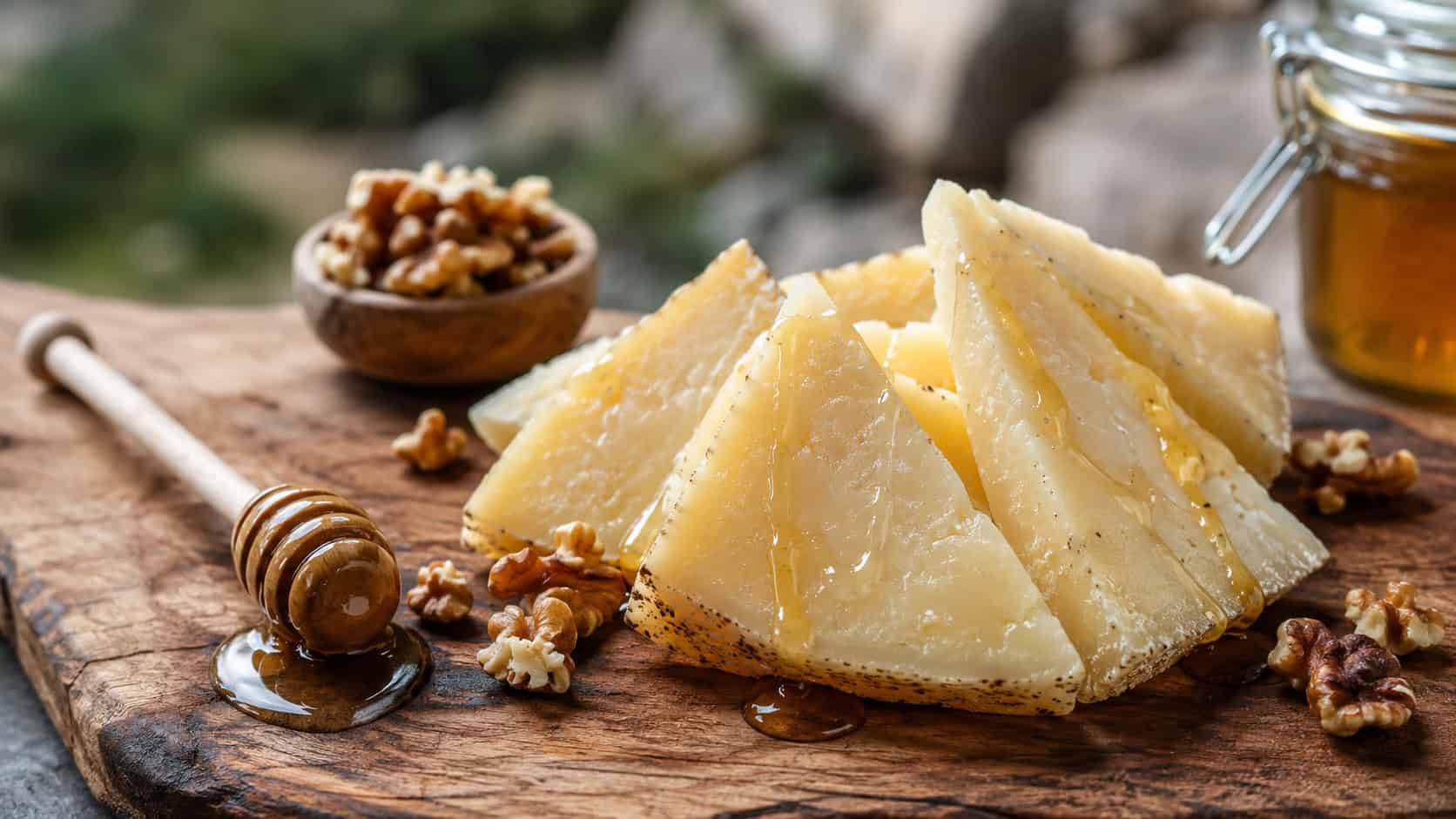 pecorino cheese wedges drizzled with honey in a wide horizontal shot, on a rustic board with toasted walnuts and a honey dipper, natural light, shallow depth of field, landscape orientation