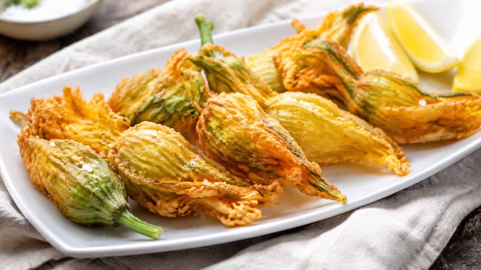 crispy fried zucchini blossoms in a wide horizontal shot, golden and delicate on a white platter with lemon wedges and sea salt, natural light, shallow depth of field, landscape orientation