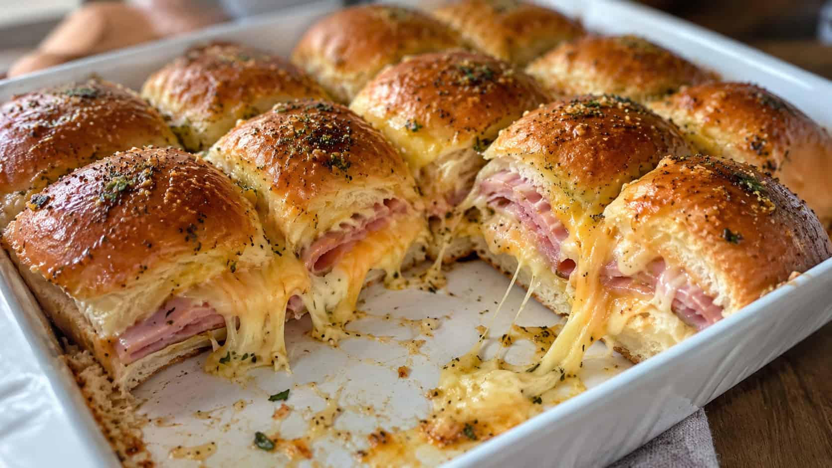 golden ham and cheese sliders pulled apart in a wide horizontal baking dish, melty cheese and glossy buttered tops, warm natural light, shallow depth of field, landscape orientation