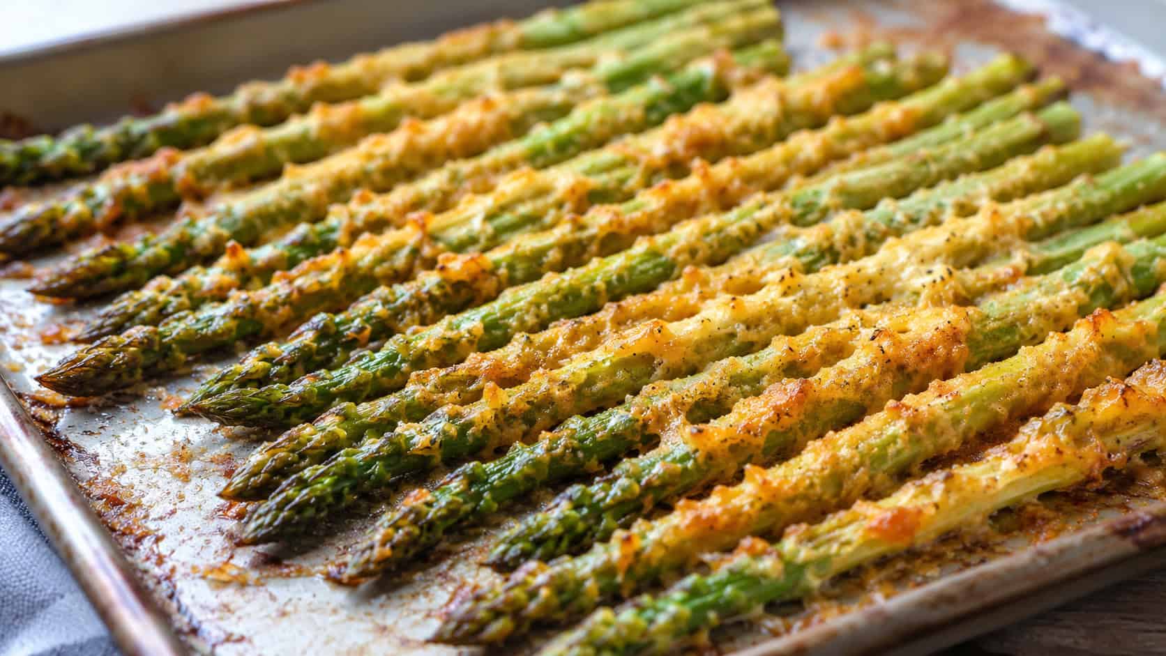 roasted Parmesan asparagus spears lined up on a wide horizontal sheet pan, crispy golden cheese coating, bright natural light, shallow depth of field, landscape orientation