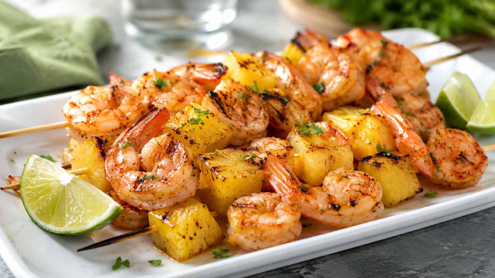 grilled pineapple and shrimp skewers arranged on a wide horizontal platter, caramelized edges and glossy glaze, lime wedges, bright natural light, shallow depth of field, landscape orientation