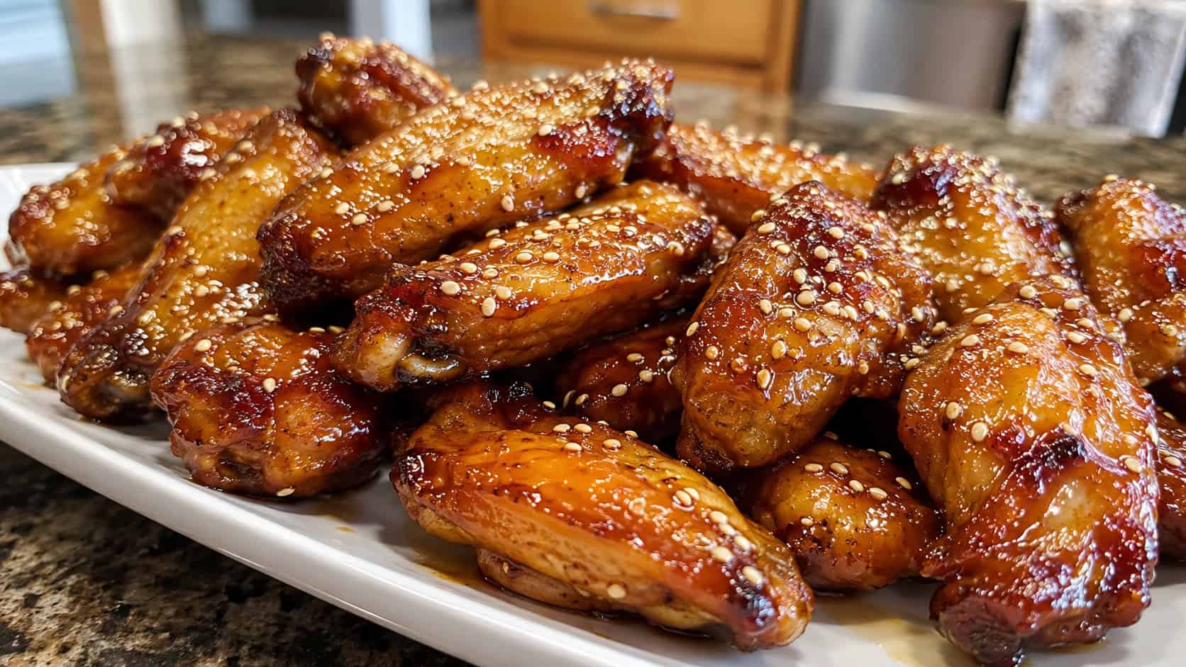 glossy honey garlic chicken wings piled on a wide horizontal platter, sticky caramelized glaze and sesame, warm natural light, shallow depth of field, landscape orientation