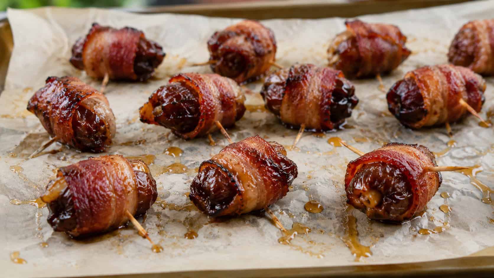 bacon-wrapped dates arranged on a wide horizontal parchment-lined tray, crispy caramelized bacon and a honey drizzle, warm natural light, shallow depth of field, landscape orientation