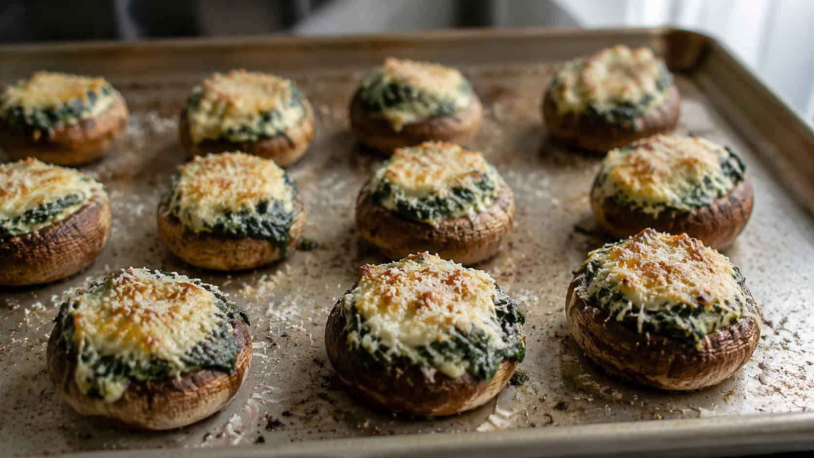 spinach-stuffed mushrooms arranged on a wide horizontal baking tray, golden bubbly cheese tops, scattered Parmesan, natural light, shallow depth of field, landscape orientation