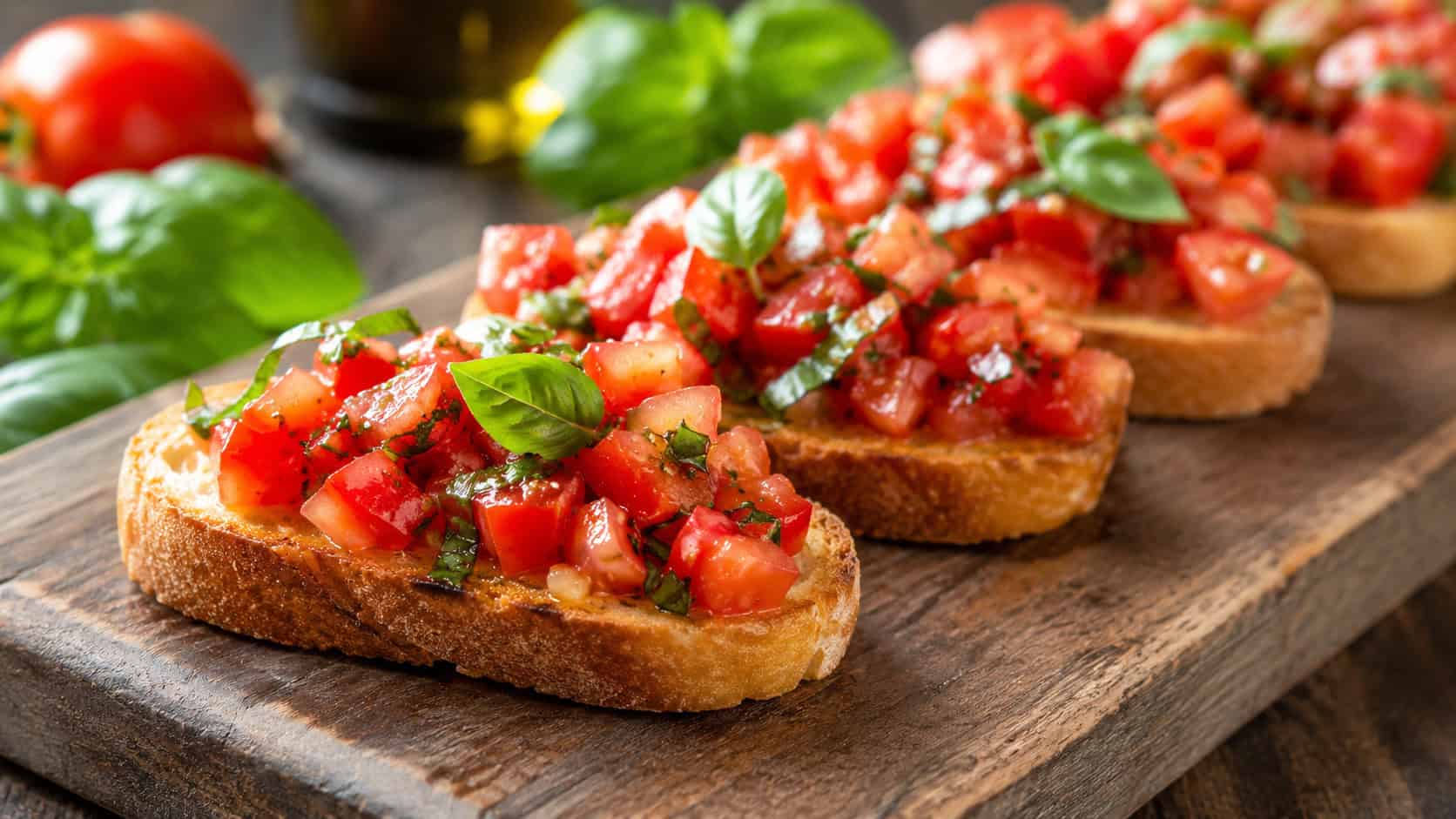tomato basil bruschetta arranged across a wide horizontal wooden serving board, juicy red tomatoes and green basil on golden toast, bright natural light, shallow depth of field, landscape orientation