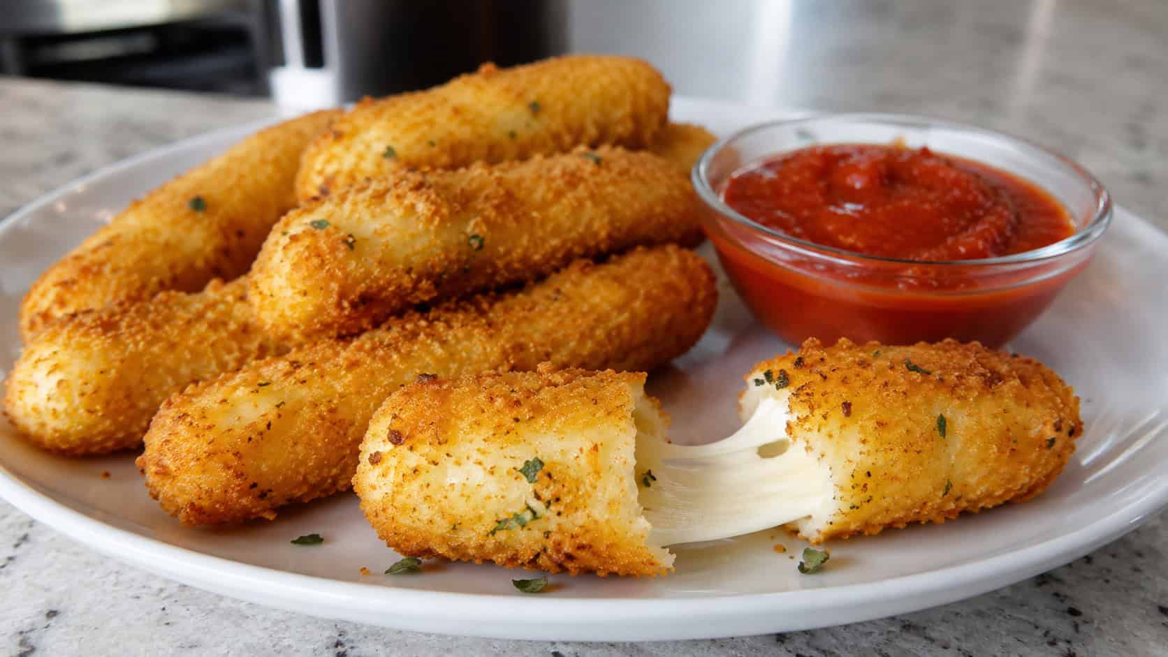 golden mozzarella sticks with one pulled apart showing melted cheese, arranged on a wide plate with marinara, set on a counter, natural light, shallow depth of field, landscape orientation